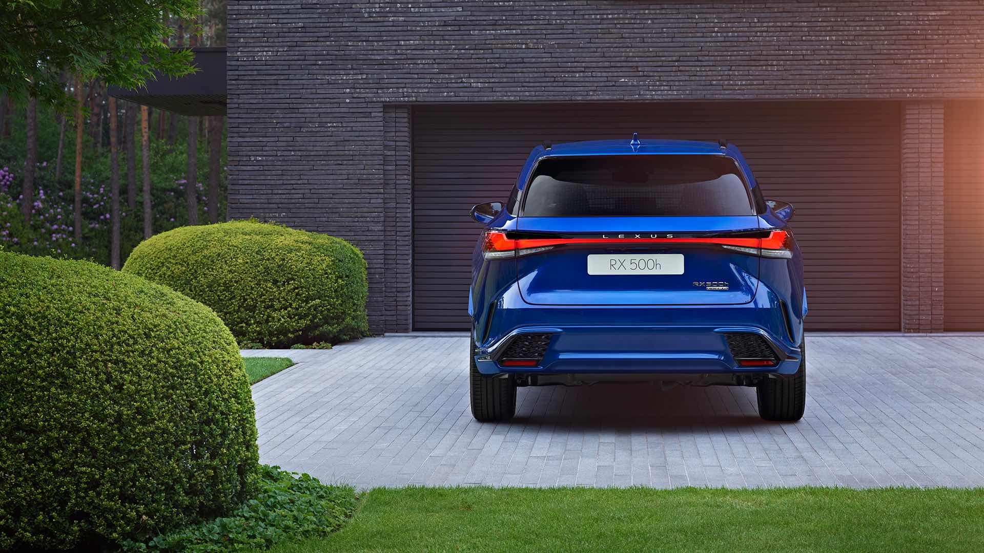 A sapphire blue Lexus RX sits on a concrete driveway. Greenery surrounds it.