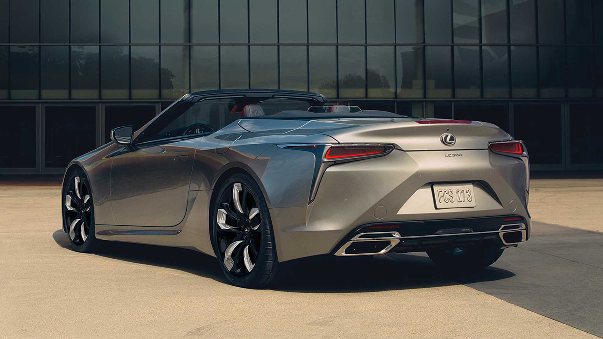 Lexus LC 500 Convertible with the roof open is shown from the rear. It is parked in front a glass walled building.