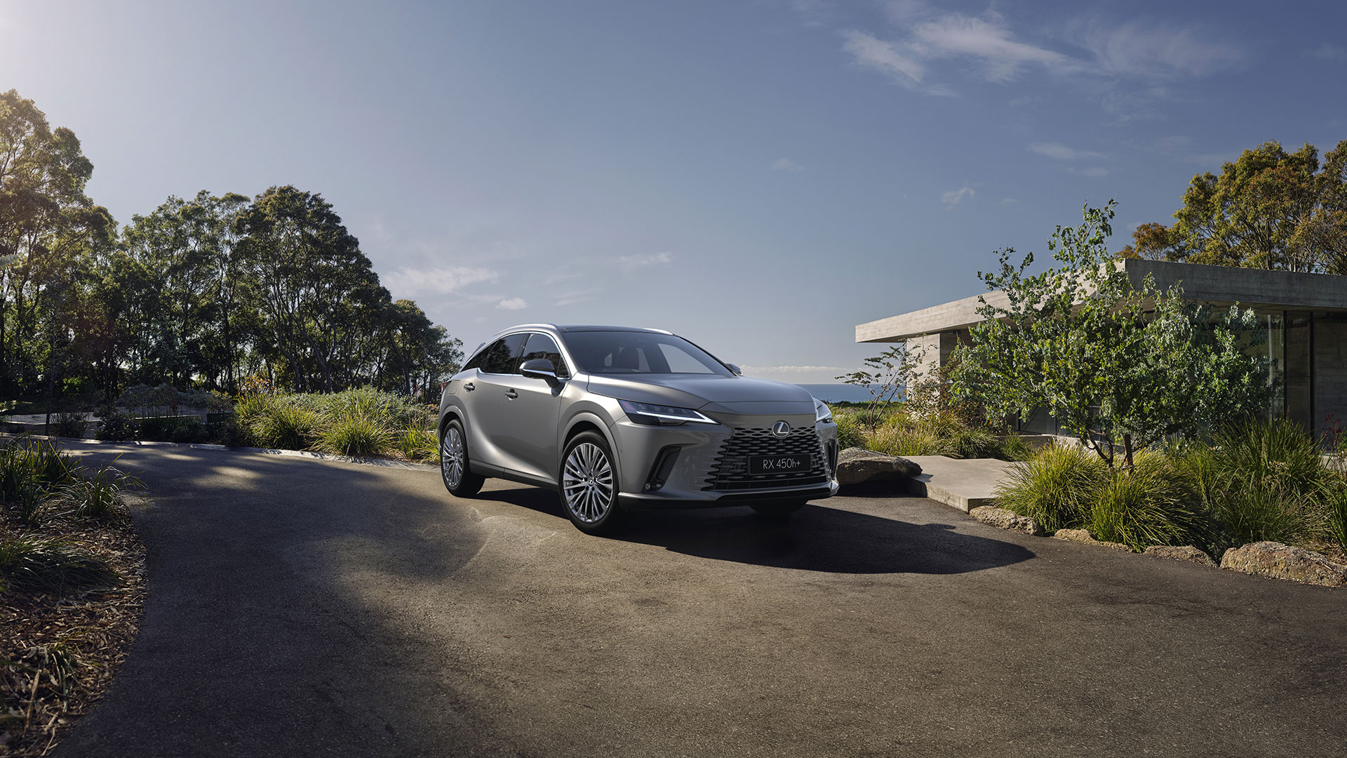 Silver Lexus RX 450h+ parked on a curved driveway beside a modern concrete building